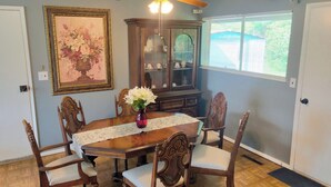 A dining room with a wooden table, six chairs, a vase with flowers, a ceiling fan, and a large mirror. - Cozy Retreat with a Fenced Yard (Huber Heights)
