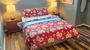 A bedroom with a bed, two bedside lamps, a nightstand, a window with blinds, a framed picture on the wall, and a wooden floor. - Cozy Retreat with a Fenced Yard (Huber Heights)