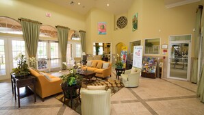 A spacious lobby with a yellow wall, a reception desk, a yellow sofa, a white armchair, and a coffee table. - Pool Home With Spa & Games Room In Gated Resort With Extensive Amenities (Davenport)