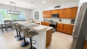 A modern kitchen with a central island, bar stools, wooden cabinets, a stainless steel refrigerator, and a microwave. - Pool Home With Spa & Games Room In Gated Resort With Extensive Amenities (Davenport)