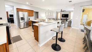 A modern kitchen with a central island, stainless steel appliances, and a dining area with bar stools. - Pool Home With Spa & Games Room In Gated Resort With Extensive Amenities (Davenport)