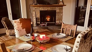 A dining room with a wooden table set for four, a fireplace, and a television above it.