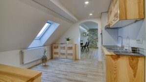 A modern kitchen with wooden cabinets, a skylight, a dining area with chairs, and a stone wall.
