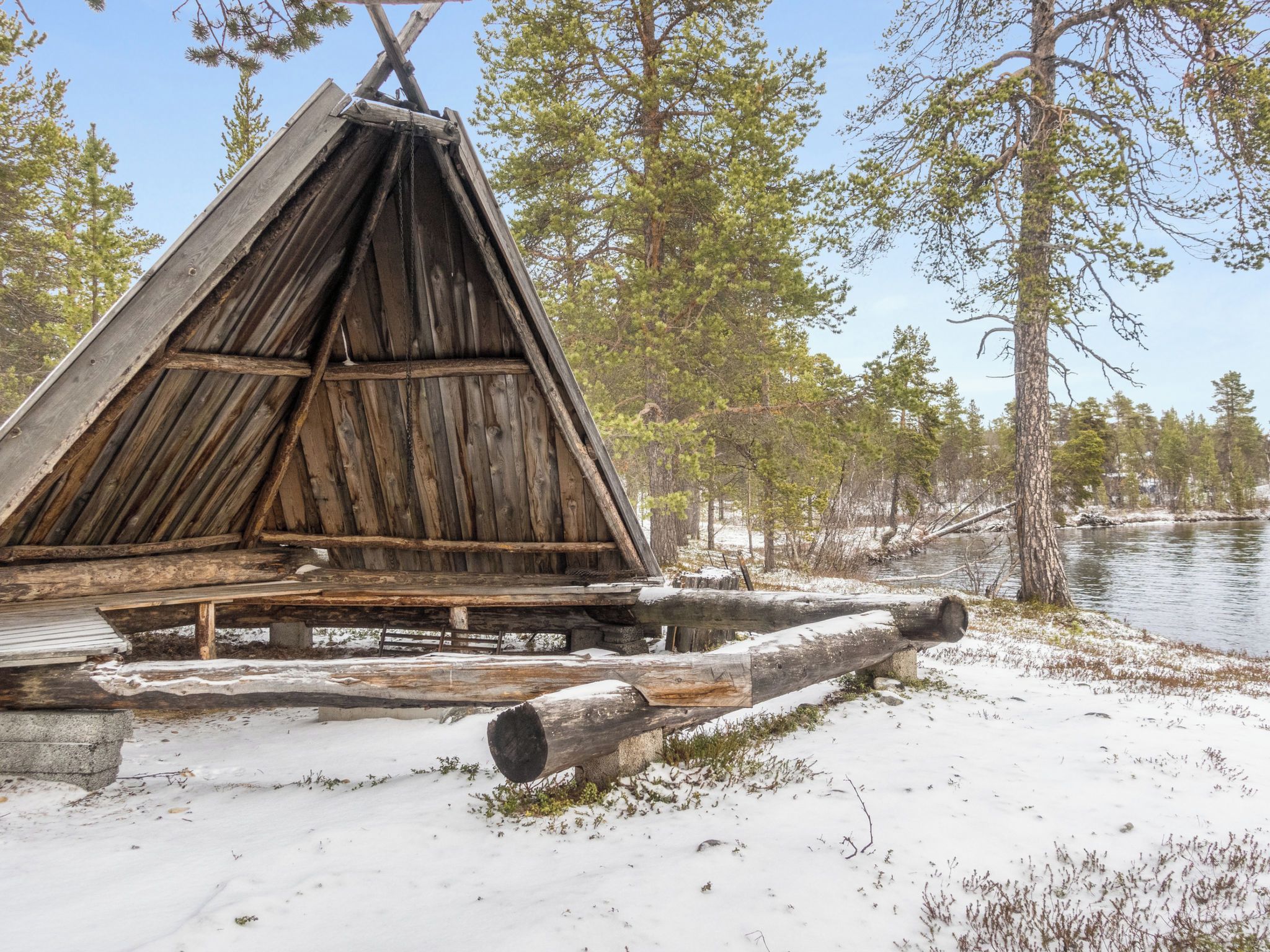 A wooden cabin with a triangular roof, surrounded by snow and trees.