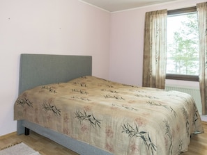 A single bed with a headboard, a window with curtains, and a wooden floor.