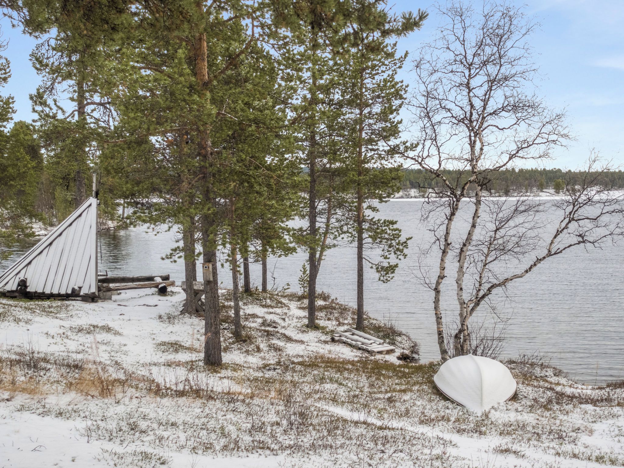 Una baita sul lago con un molo in legno, circondata da alberi e terreno innevato.