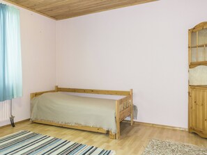 A single bed in a room with wooden flooring, a window with blue curtains, and a wooden cabinet. - Vacation home Danila by Interhome (Inari)