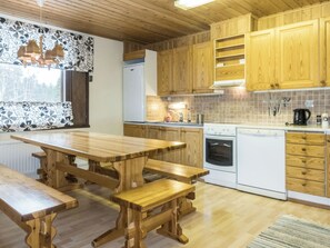 A kitchen with wooden cabinets, a white stove, a sink, and a large wooden table with benches. - Vacation home Danila by Interhome (Inari)