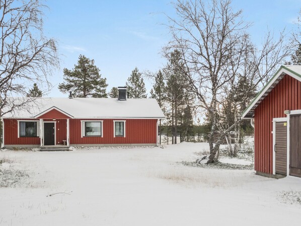 Ett rött, envåningshus med ett snötäckt tak, en veranda och ett garage.