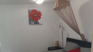 A bedroom with a bed, a nightstand, a lamp, a red flower painting, and a ceiling fan.