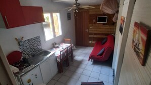A compact kitchen with a dining area, a ceiling fan, and a small seating area with a red chair.