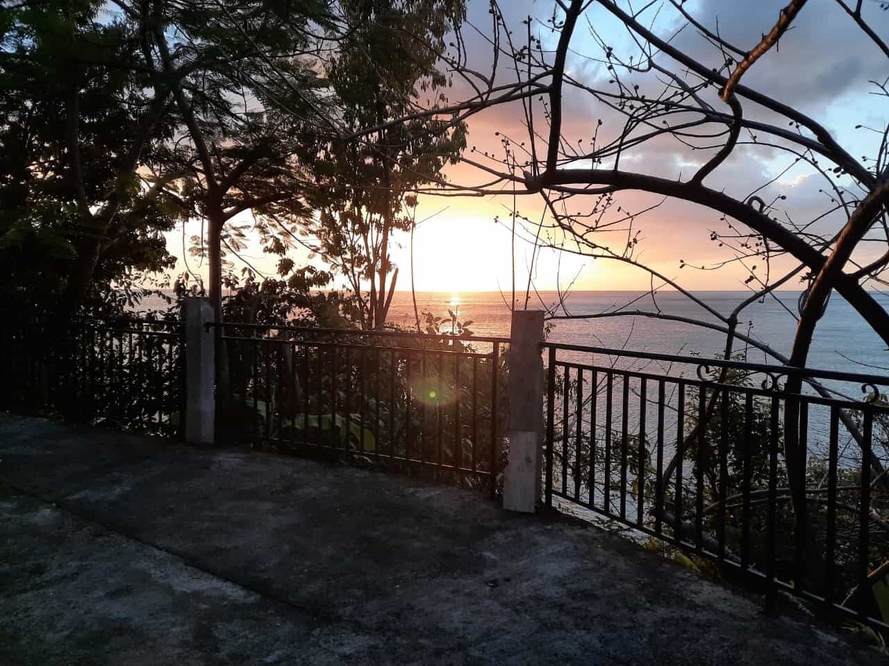 A sunset view from a balcony with a metal railing and concrete pillars.