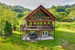 A two-story wooden house with a balcony, surrounded by lush greenery. - Cruizin River Dreams- Riverfront, fire pit, hot tub (Todd)