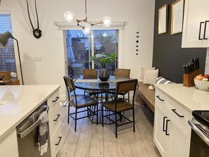 A modern kitchen with a dining table, chairs, and a chandelier. There is a window with a view of the outside.