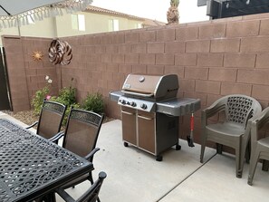 A patio with a barbecue grill, outdoor chairs, and a table.
