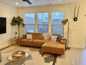 A living room with a brown sofa, a large plant, a TV, and a wall-mounted lamp.