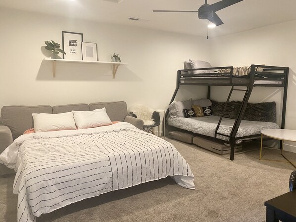 A bedroom with a bunk bed, a sofa, a small table, and a ceiling fan.