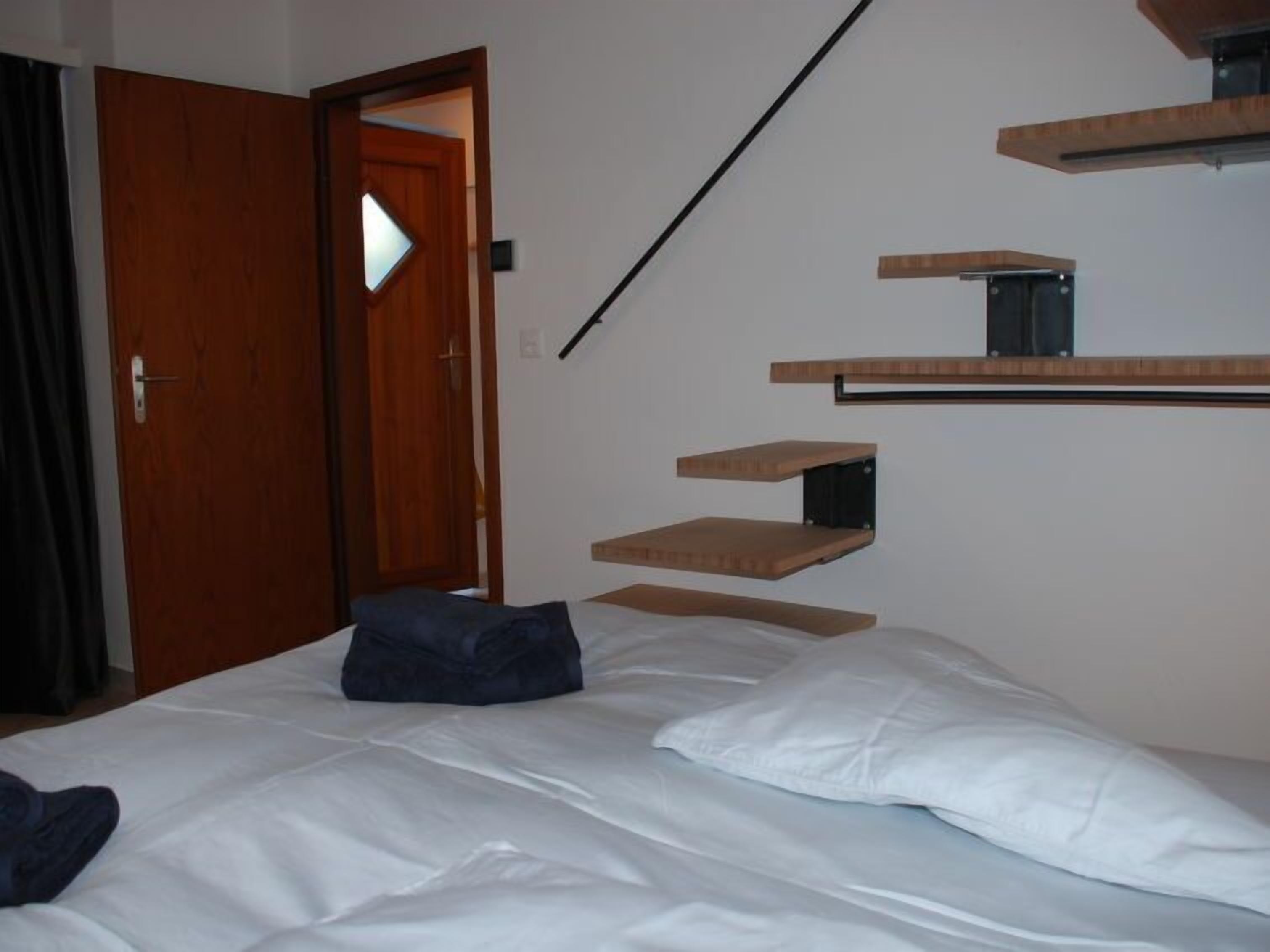 Een slaapkamer met een bed, een houten deur en een trap met ingebouwde planken.