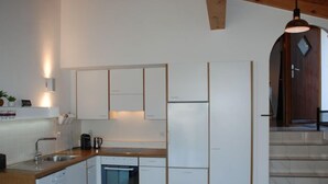 Une cuisine moderne avec des armoires blanches, un plan de travail en bois, un four encastré et une machine à café.