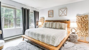 A bedroom with a large bed, a window with curtains, a wooden headboard, and a rug. - Sterling Valley Home ~ 9 Mi to Stowe Mountain! (Morristown)
