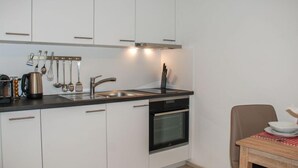 A modern kitchen with white cabinets, a black countertop, a sink, a stove, and a dining table with a chair. - Appartamento 2- Giardino by Interhome (Locarno)