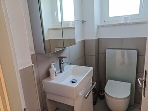 A compact bathroom with a white sink, a mirror, a toilet, and a window. - Appartamento 2- Giardino by Interhome (Locarno)