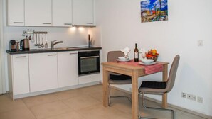 A compact kitchen with white cabinets, a built-in oven, and a dining table with chairs. - Appartamento 2- Giardino by Interhome (Locarno)