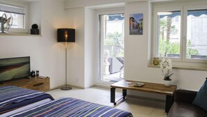 A modern bedroom with a bed, a desk, a lamp, and a window with a view of greenery. - Appartamento 2- Giardino by Interhome (Locarno)