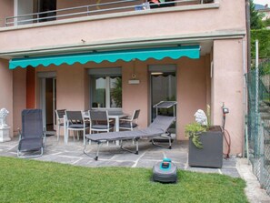 A patio with a table and chairs, a lounge chair, and a small garden area with a lawnmower. - Appartamento 2- Giardino by Interhome (Locarno)