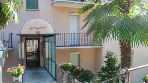 A building entrance with a curved awning, a metal gate, and a small balcony with plants. - Appartamento 2- Giardino by Interhome (Locarno)