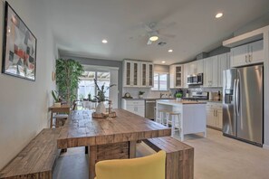 A modern kitchen with white cabinets, stainless steel appliances, and a wooden dining table. - Desert Hot Springs Home w/ Pool & Gas Grill! (Desert Hot Springs)