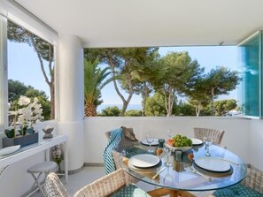 Ein stilvoller Essbereich mit einem Glastisch, Korbstühlen und Blick auf Bäume und das Meer.