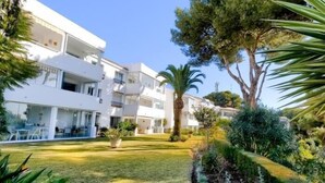 A modern multi-story building with balconies, surrounded by well-maintained gardens and trees.