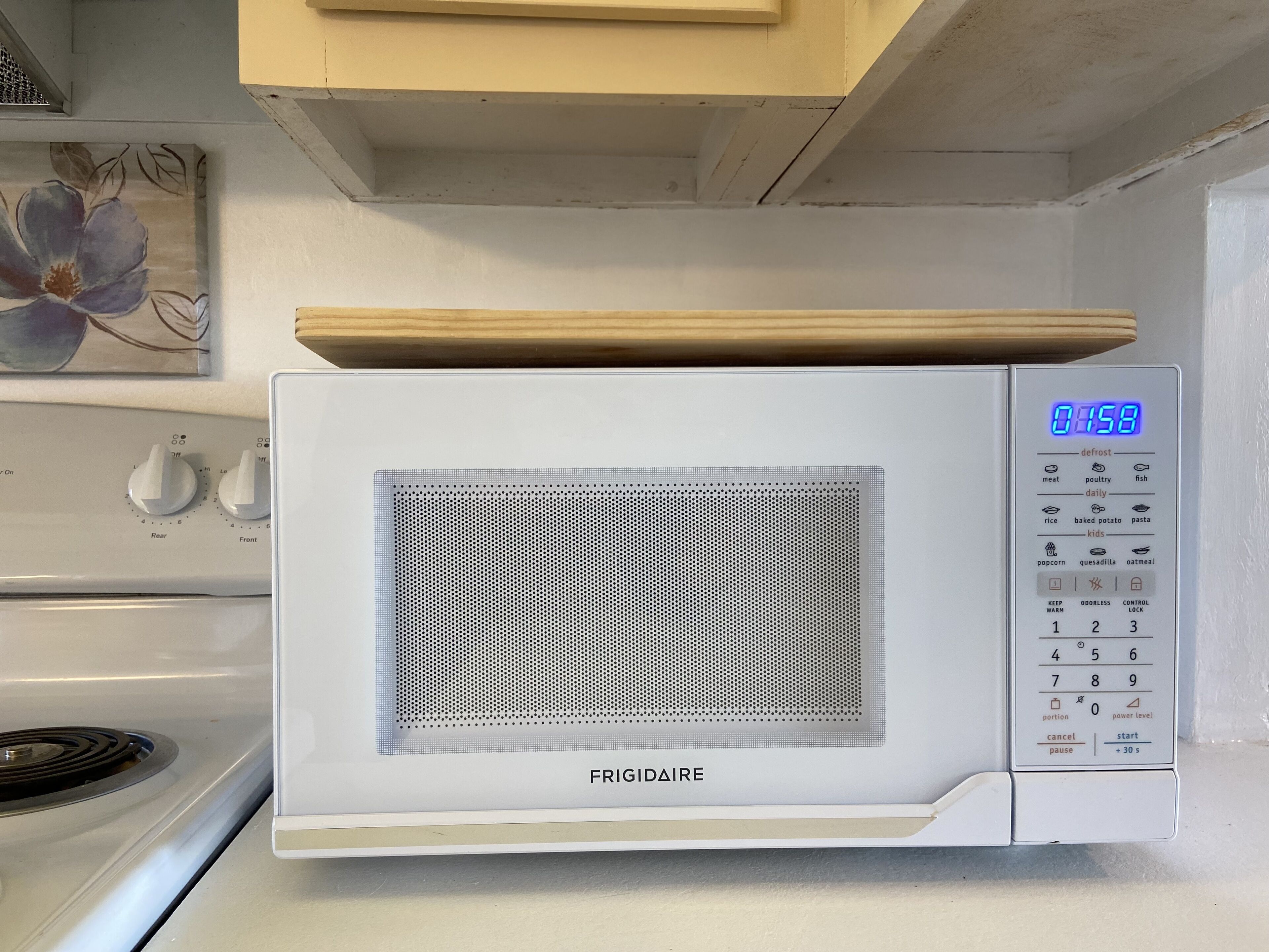 Un four à micro-ondes FRIGIDAIRE blanc, doté d’un écran numérique, d’un panneau de commande et d’une porte en verre perforée.