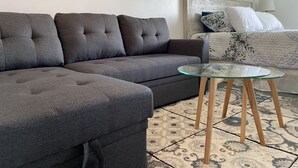 Uma sala de estar moderna com um sofá seccional cinza, uma mesa de centro de vidro e um tapete estampado.