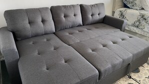 Um sofá modular cinzento com design acolchoado, posicionado em um quarto com uma cama e um espelho na parede.