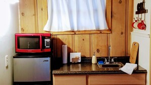 Eine kleine Küche mit Holzausstattung, einer integrierten Mikrowelle, einem Kühlschrank, einem Spülbecken und einem Fenster mit Vorhängen.