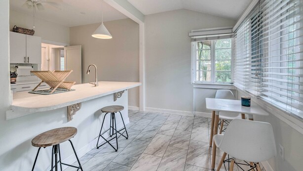 Une cuisine moderne avec un plan de travail blanc, des tabourets de bar et un coin repas comprenant une table et des chaises.