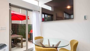 A modern room with a glass table and yellow chairs, a sliding glass door leading to an outdoor area with a red umbrella, and a large mirror on the wall. - Walkable in Heart of Ballard (Seattle)