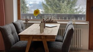 Un comedor con una mesa de madera y dos sillas grises tapizadas. Un jarrón con una flor amarilla está sobre la mesa.