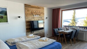 Una habitación moderna con cama, televisor, zona de comedor y vistas al exterior.