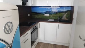 Una cocina compacta con armarios blancos, horno integrado y un lavabo.