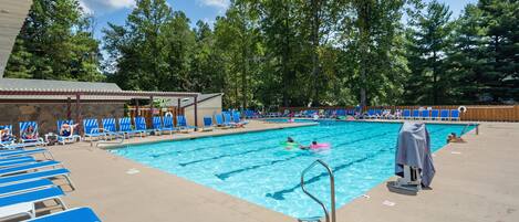 A swimming pool with blue lounge chairs, a covered area, and trees in the background.