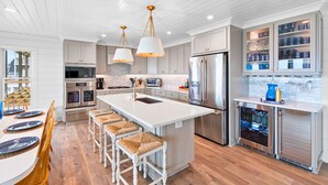 A modern kitchen with white cabinetry, stainless steel appliances, and a central island with bar stools. - "Porpoise Point" - Oceanfront Home, 5 Bedrooms / 5 Bathrooms, w/ PRIVATE POOL (Holden Beach)