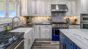 A modern kitchen with white cabinets, a blue stove, and a large window. - "All Hands On Deck" Oceanfront with elevator 5 bedrooms, 5 bathrooms. (Holden Beach)