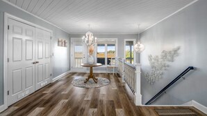 A spacious hallway with wooden flooring, a round table with a vase, white doors, and a staircase with a railing. - "All Hands On Deck" Oceanfront with elevator 5 bedrooms, 5 bathrooms. (Holden Beach)