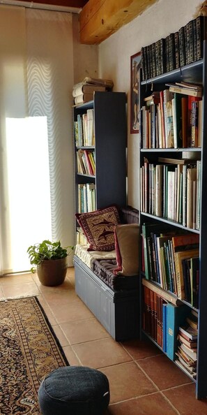 Relax in a cozy reading nook with a comfortable armchair and side table, surrounded by a bookshelf and lush greenery.