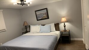 A bedroom with a bed, two bedside lamps, a ceiling light fixture, and a framed picture on the wall.