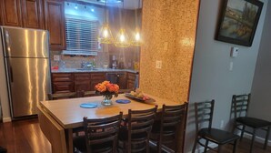 A modern kitchen with wooden cabinets, a stainless steel refrigerator, and a dining area with a wooden table and chairs.