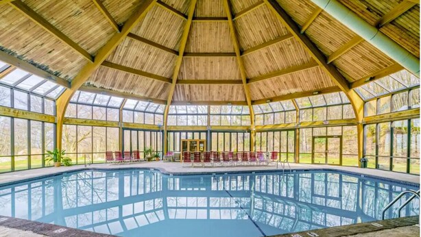 An indoor swimming pool with a glass ceiling and a wooden deck area.